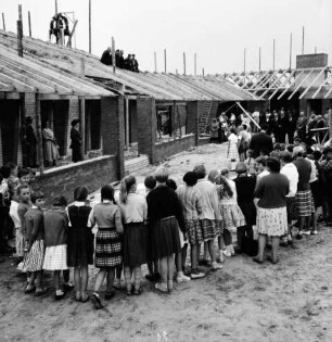 Volksschule: Neubau: Rohbau: Richtfest: vorn Schülerhalbkreis: rechts dahinter Funktionsträger: hinten Pavillonbauten mit Richtkrone und Arbeitern auf Dachsparren