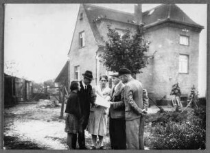 Personengruppe vor einem Haus stehend über ein Papier gebeugt