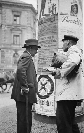 Männer im Gespräch vor einer Litaßsäule mit Wahlwerbung der Partei "Der Mittelstand" und der NSDAP