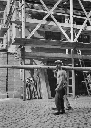 Arbeiter beim Transport einer hölzernen Gerüstleiter auf einer Baustelle vor einem bereits montierten Leitergerüst : Leipzig. Arbeiter beim Transport einer hölzernen Gerüstleiter auf einer Baustelle vor einem bereits montierten Leitergerüst