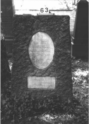 Grabstein 63 (Index: 100081670) Material: Granit, weiße Marmorplatte Zustand: gut Maße HxBxT: 140x84x37 cm Beschreibung: leicht konische Stele, gerader Abschluß, ovale und querrechteckige Schriftplatte: Grabstein 63