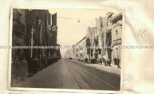 Mit Hakenkreuzfahnen geschmückte Straße und Passanten in Lodz