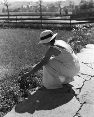Frau, an der Randbeplanzung eines gepflasterten Gartenweges hockend