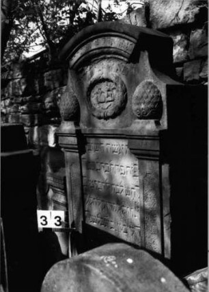 Grabstein 33 (Index: 99629534) Material: Sandstein Zustand: verwittert/Textverlust Maße HxBxT: 178x67x16 cm Beschreibung: Stele mit eingezogenem Segmentbogenabschluß mit Verdachung, zwei Pilaster Symbolik: Kranz, zwei Pilaster mit Pinienzapfen Besonderheit: Zitat Proverbia 31, 26: Grabstein 33