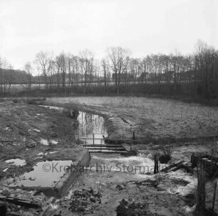 Lasbek-Gut: Mühlenbach: Mauerreste mit Steg nach Abriss der Lasbeker Mühle: hinten Baumreihe: dahinter Häuser