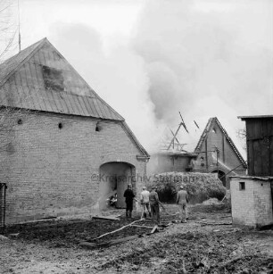 Brand: Wohn- und Wirtschaftsgebäude von Landwirt Leinius: links rauchende Scheune : dahinter brennendes Wirtschaftsgebäude: im Vordergrund Feuerwehrmann und weitere Männer mit Wasserschläuchen