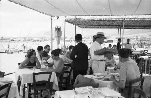 Glyfada: Publikum bei Tisch, Verkäufer drauf