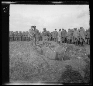 [Bailleul-Sir-Berthoult (Dep. Pas-de-Calais, Frankreich):] Offiziere mit Schirmmützen und Soldaten mit Feldmützen und Pickelhauben auf einem Feld ("Schießplatz") bei 4 in einem Graben stehenden Offizieren mit Schirmmützen