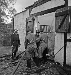 Schleushörn: Brand: Trabergestüt und Reitstall "Schleushörn" von Klaus Martens: brennender Stall mit Reetdach: vorn vier Feuerwehrmänner beim Löschen durch Eingang