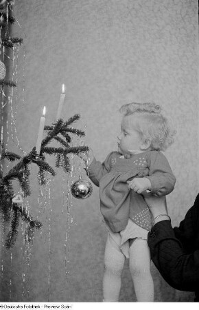 Porträt eines kleinen Mädchens mit Christbaumkugel an einem Weihnachtsbaum