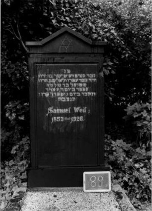 Grabstein 89 (Index: 100110345) Material: Granit Zustand: gut Maße HxBxT: 148x68x19 cm Beschreibung: Stele, Sockel, eingezogener giebelartiger Abschluß mit Verdachung Symbolik: Davidstern Steinmetz: H. Mayer: Grabstein 89