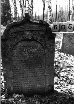 Grabstein 605 (Index: 99753117) Material: Sandstein Zustand: verwittert Maße HxBxT: 109x65x11 cm Beschreibung: Stele, eingezog. Kielbogenabschl. , Schrift eingetieft mit eingezog. Rundbogenabschl. Symbolik: Blätter, Schriftband: Grabstein 605