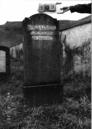 Grabstein 109 (Index: 99798502) Material: Kunststein Zustand: gut Maße HxBxT: 130x50x15 cm Beschreibung: Stele mit doppelt eingezogenem Rundbogen, Sockel: Grabstein 109