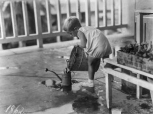 Ein Kind : Kind beim Befüllen einer Gießkanne mit einem Eimer