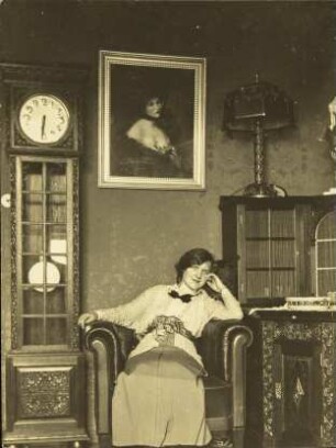 [Frau auf einem Sessel neben einer Standuhr]