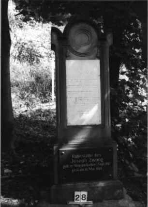 Grabstein 28 (Index: 100079863) Material: Sandstein, weiße Marmorplatte, schwarze Granitplatte Zustand: gut Maße HxBxT: 188x60x32 cm Beschreibung: Stele, getreppter Sockel, Rundbogenabschluß mit ausgezogenen Eckakroteren, zwei rechteckige Schriftplatten Symbolik: Blüten: Grabstein 28