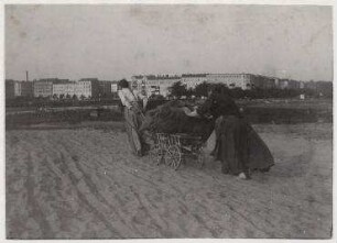 Ohne Titel (Zwei Frauen ziehen und schieben gemeinsam den Handkarren durch den Sand, Blick auf die Knobelsdorffbrücke)