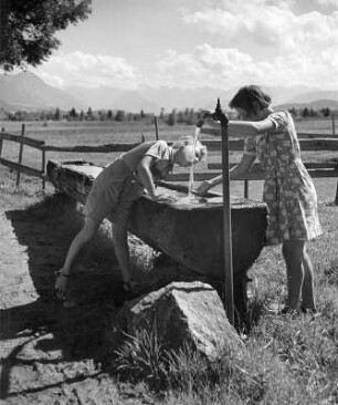 Kinderbilder. Allgäu. Geschwisterpaar bei einer Rast an einer Koppel. Die Schwester den Hahn eines Wassertroges aufdrehend, der Bruder trinkend