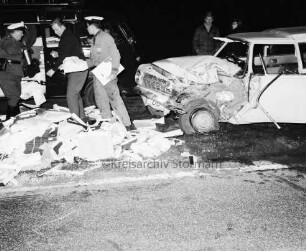 B 404: bei Tralau: Verkehrsunfall: Zusammenstoß von Pkw-Kombi mit Lkw: Pkw-Kombi mit eingedrückter Front: davor auf Fahrbahn zahlreiche Pakete von Ladung: Polizist, zwei Männer, Einsatzwagen von Rettungskommando mit geöffneter Seitentür: hinten Zuschauer: im Dunkeln, 12. Januar 1965