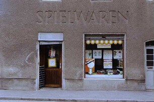 DDR. Erdgeschoß eines Wohnhauses mit Ladeneinbau und Inschrift "Spielwaren", genutzt als Konsum-Gemüseladen. Eingang und Schaufenster