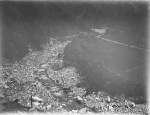 Flussbett : Blick in ein wenig Wasser führendes Flussbett, rechts davon Straße und Siedlung