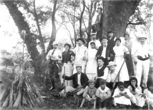 Gruppenbild einer Jagdgruppe mit Ernst Otto Gerhardt und einheimischen Jagdhelfern sowie Begleittross am Lagerfeuer, aufgenommen in Argentinien