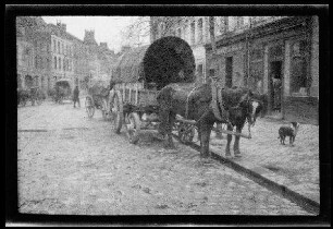 Nicht identifizierbare Ortschaft in Nordfrankreich oder Belgien: Zweispänner mit Planwagen am Rand einer gepflasterten Ortsstraße