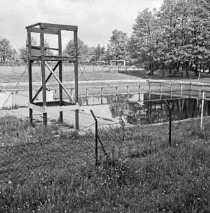 Freibad: links Gerüst des ehemaligen Sprungturms: dahinter Schwimmbecken: vorn beschädigter Maschendrahtzaun: im Hintergrund links Sportplatz: rechts Bäume