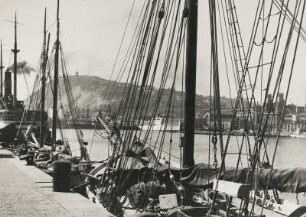 Spanien. Hafenstadt Barcelona. Blick vom Handelshafen zum Tibidabo, einem der Hausberge der Hafenstadt. Am Kai angelegte Segelboote