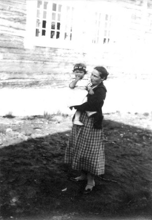 Photographien von Lappland. Junge Mutter, ihre kleine Tochter mit Blütenkranz auf dem Kopf auf dem Arm haltend