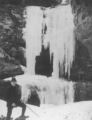 Sächsische Schweiz, Großer Zschand. Weberschlucht. Wanderer mit Spazierstock in der Felsgrotte mit gefrorenem Wasserfall