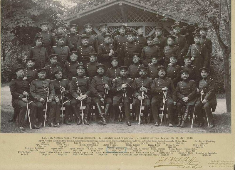 Teilnehmer (ca. siebenunddreissig Personen) am Lehrkurs der Infanterie-Schiessschule Spandau vor Waldhütte teils stehend, teils sitzend