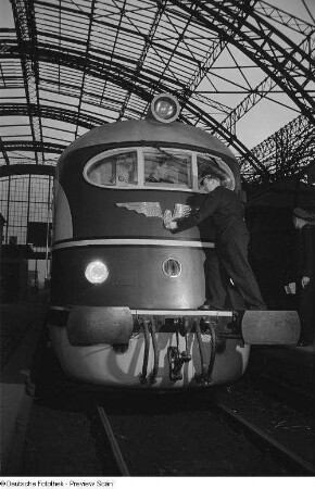Bahnarbeiter beim Säubern des Logos der Deutschen Reichsbahn an einer Schnellzuglokomotive