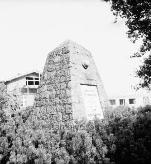 Dorfstraße: Ehrenmal: vorn Tannen: rechts oben Baumäste: hinten Häuser