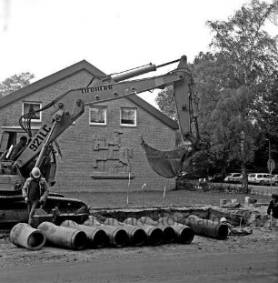 Abwasser: Ausbau der Kanalisation: Wöhrendamm: vorn Röhren: dahinter Baugrube: links Arbeiter und Bagger: rechts weiterer Arbeiter: hinten links Waldreitersaal mit Relief an Giebelfront: hinten rechts parkende Pkws und Bäume