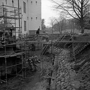 Restaurierung: Sanierung Mauerwerk an Turmfuß: Arbeiter auf Gerüst, Schubkarren: innerer Graben: neue Grabenversteifung mit Holzbohlen am Grabenfuß: Grabenböschung nach Wiederherstellung mit alten Findlingen: im Hintergrund Lübecker Straße, Bauernbrücke, Kastanienallee