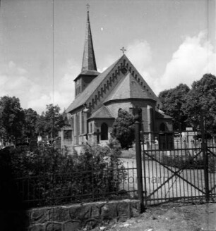 Evangelische Kirche: Außenansicht von Osten: davor Kirchhof: vorn Mauer mit Zaun und Gatter: hinten Bäume