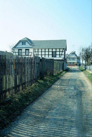 Weg entlang eines langen Staketenzauns, hinten Gehöft