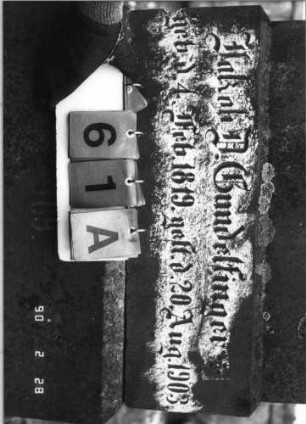 Grabstein 61 (Index: 100114623) Material: Sandstein Zustand: Stele verrutscht, Textplatte fehlt Maße HxBxT: 258x70x29 cm Beschreibung: Ädikula mit Sockel auf Rustikasockel, überstehender, eingezogener Rundbogen mit Konche und Akroteren, eingesetzte Textplatte Symbolik: Konche: Grabstein 61A