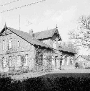 Volksschule mit Schulhof: vorn Hecke: rechts Baumäste: hinten rechts Haus