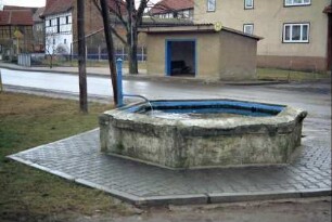 sechseckiger flacher Laufbrunnen, Bushaltestelle, Häuser