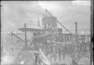 Passagiere an Deck des Hochseepassagierdampfers "Bremen" beobachten Mechaniker, die an dem an Haken hängenden Katapultflugzeug HE 12 D-1717 arbeiten