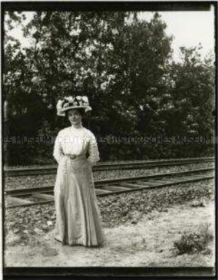 Dame mit auffälligem Hut vor einem Bahngleis