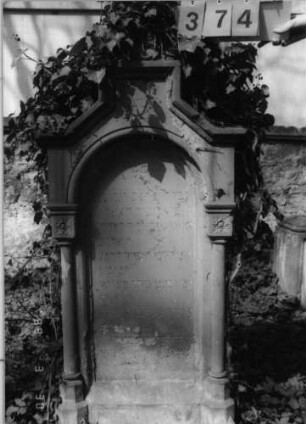 Grabstein 374 (Index: 99791775) Material: Sandstein Zustand: verwittert und abgeblättert mit Textverlust Maße HxBxT: 148x68x27 cm Beschreibung: ädikulaartige Stele mit Säulen, Sockel, eingezogener giebelartiger Abschluß, rechteckig erhöht, Schriftfeld eingetieft mit Rundbogenabschluß Symbolik: Blüten: Grabstein 374