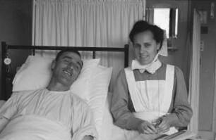 Zweiter Weltkrieg. Lazarett (wahrscheinlich in Holland). Verwundeter Angehöriger der deutschen Wehrmacht im Krankenhausbett. Daneben eine Krankenschwester
