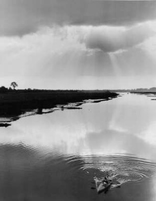 Impression. Die Sonne bricht durch die Wolken und spiegelt sich in dere Süderelbe. Ein Ruderboot befindet sich auf dem Gewässer