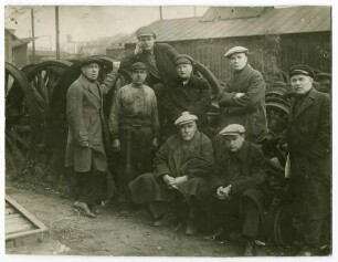 Kampfgruppe (acht Personen) der Eisenbahnarbeiter 1905- Rotearmee-Partisan 1917 in Charkow, teils stehend, teils sitzend vor Eisenbahn-Laufrädern