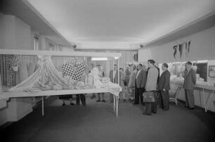 Besucher der Leipziger Herbstmesse 1955 betrachten drapierte Stoffbahnen