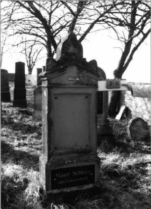Grabstein 76 (Index: 100116219) Material: Sandstein, Granitplatte Zustand: Schriftplatte an der Stele fehlt, sonst gut Maße HxBxT: 190x57x27 cm Beschreibung: aufgesockelte Stele mit Giebelabschluß, Eckakroteren und Aufsatz, Schriftplatte auf Stele und oberem Sockel: Grabstein 76