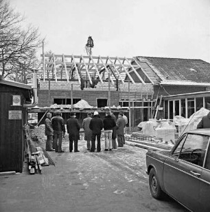 Volkshochschule Barsbüttel-Stellau: Erweiterungsbau: Richtfest: hinten Gebäudeteil mit Richtkrone: rechts altes Gebäude: davor Gäste: links Baubude: rechts Pkw: dahinter Baumaterial: Winter